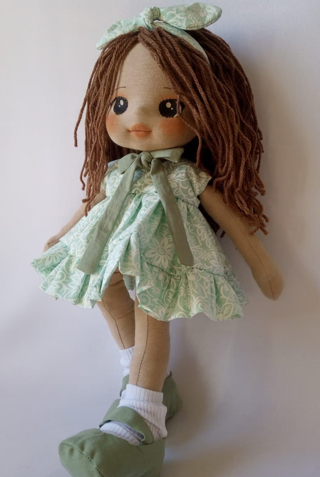 Boneca de pano morena com vestido verde claro, sapatos verde escuro e cabelo castanho