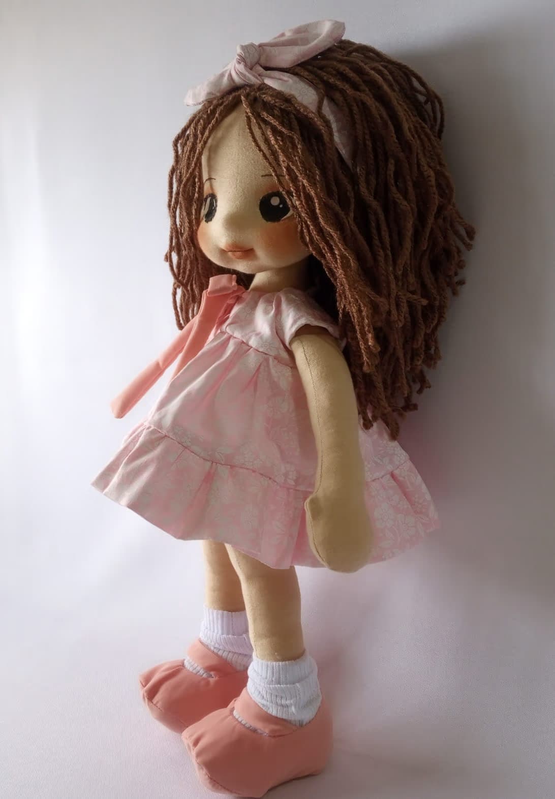 Boneca de pano morena com vestido rosa claro, sapatos rosa escuro e cabelo castanho