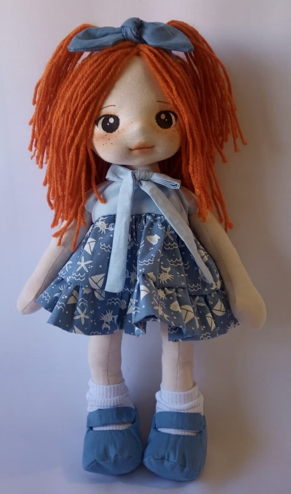 Boneca de pano ruiva com vestido azul marinho, sapato azul escuro e laço azul escuro.
