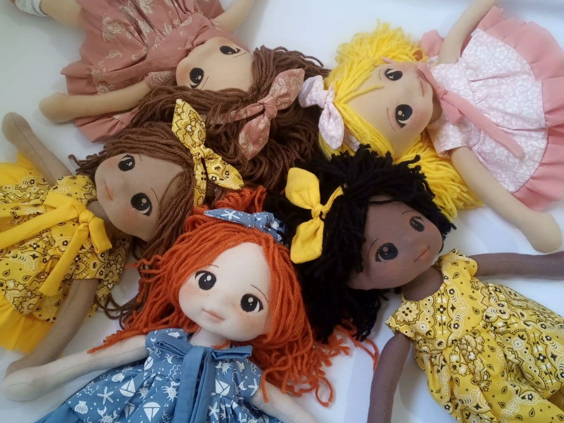 Cinco bonecas de pano de diferentes etnias em um círculo, um boneca negra, uma ruiva, uma loira, uma morena e um branca.